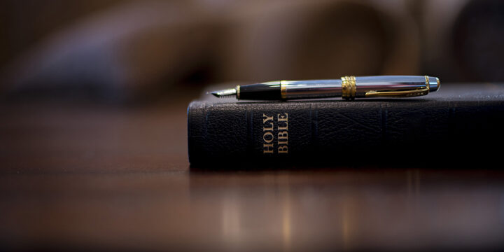 A closeup shot of the holy bible with a fountain pen on top and a blurred background